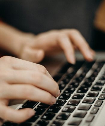 Close-up shot of hands typing on a laptop keyboard in a work environment.